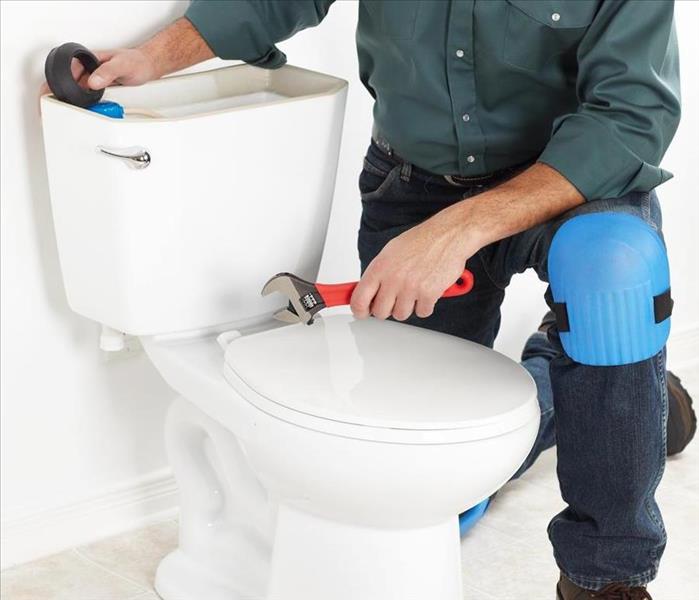 A person repairing a water leak from a toilet.