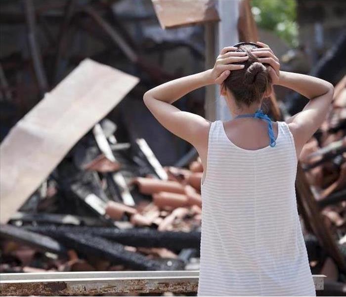 Woman holding her head watching a home destroyed by fire. 