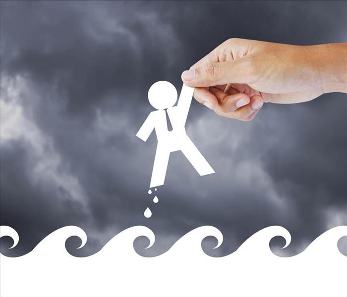 Image of person holding a paper cut shaped person on top of paper cut shaped like waves.